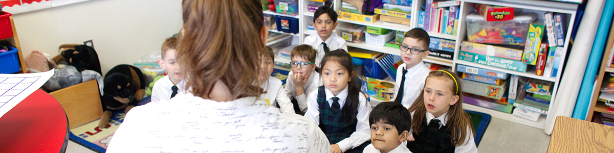 Back of teacher's head in primary classroom with students seated together facing the teacher